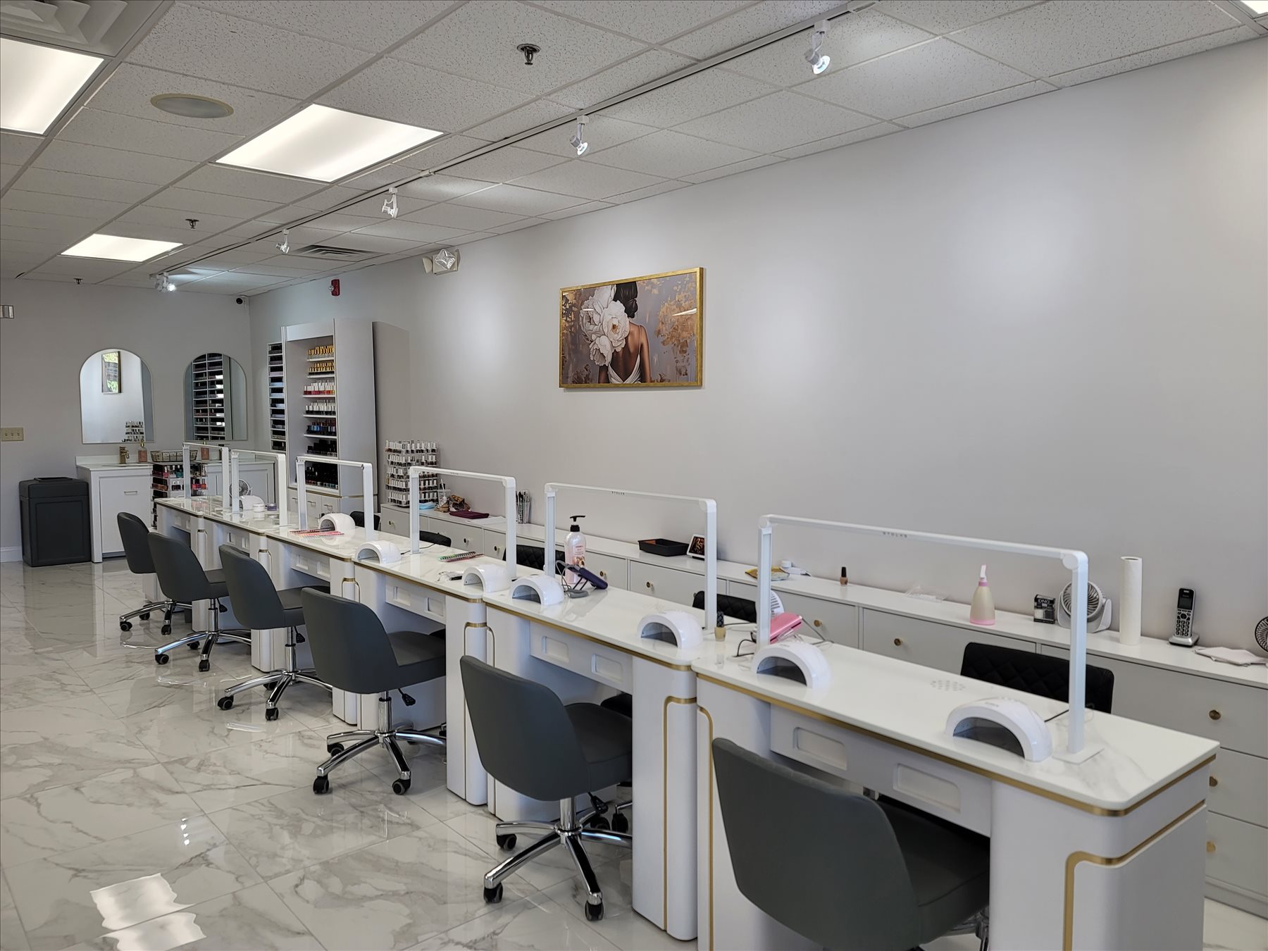 Nail Gallery manicure stations in East Lyme, CT — white-and-gold desks with UV lamps, gray swivel chairs and marble flooring